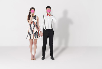 Couple holding paper hearts against white background.