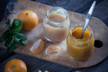 Glass jars with natural baby food with tangerine on the wooden t