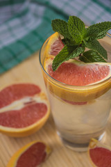 Water with ice, green mint and red orange in a glass