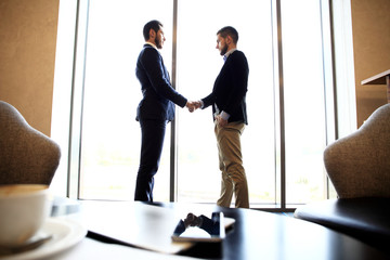 tablet computer, coffee and smartphone with businessmen handshaking on background