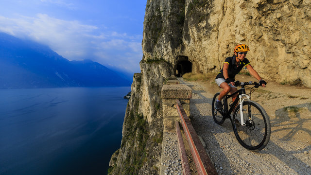 Mountain biking at sunrise woman over Lake Garda on path Sentier