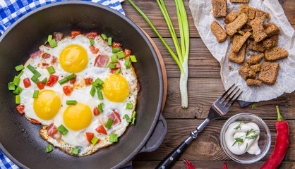 Fred eggs in pan with tomatoes and green fresh onion.