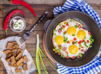 Fred eggs in pan with tomatoes and green fresh onion.