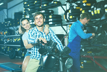 couple sitting on new motorbike in workshop.