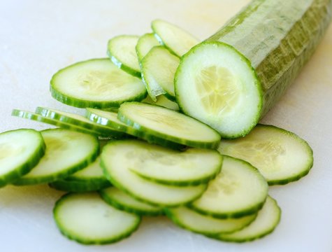 Chopped cucumber into small slices on white cutting board.