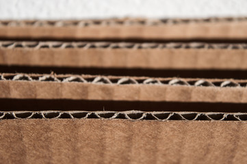 Texture of layered brown cardboard side. Folded cardboard boxes against white grunge painted wall. Wavy paper texture on sunlight with copy space.