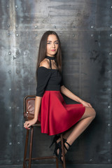 Fototapeta na wymiar Beautiful woman in a short dress sits on a chair beside the wall
