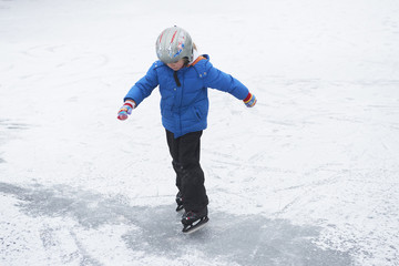 Fototapeta na wymiar Adorable little child girl ice skating in winter snow day outdoors in the park on frozen pond. Wearing safety helmet