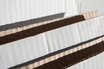Texture of layered white brown cardboard side. Folded cardboard boxes against white grunge painted wall. Wavy paper texture on sunlight with copy space.