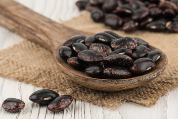 Obraz premium Black beans in a wooden spoon on old wooden table.