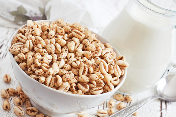 Puffed wheat cereal in white bowl with pitcher of milk in background