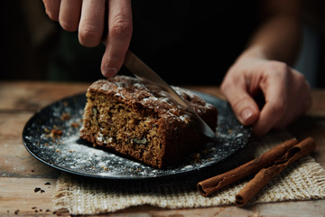 Holiday nut and cinnamon pie on dark food in rustic kitchen. Closeup of female hands cutting brown sweet cake. 