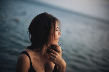 Sexy young woman in the black dress posing by the sea