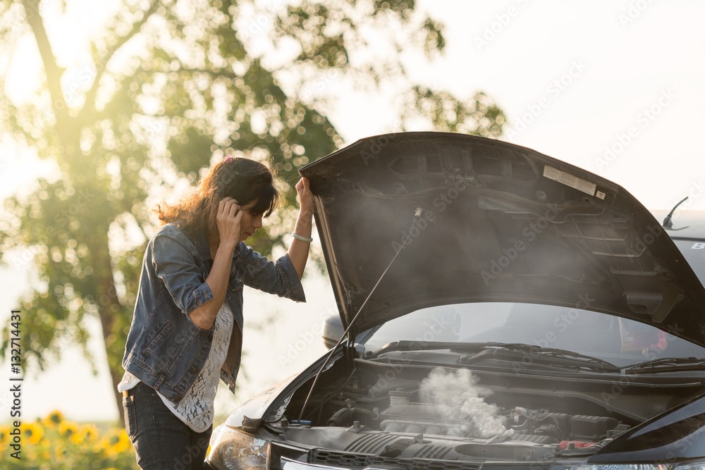 Wall mural sad woman standing on the road by the broken car in the middle of nowhere. smoke coming out the engi