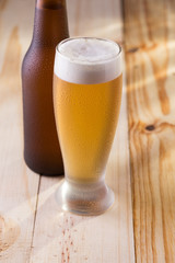 Tulipa de cerveja gelada e garrafa em mesa de madeira