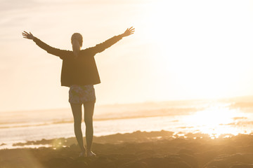 Silhouette of free woman enjoying freedom feeling happy at beach at sunset. Serene relaxing woman in pure happiness and elated enjoyment with arms raised outstretched up. 