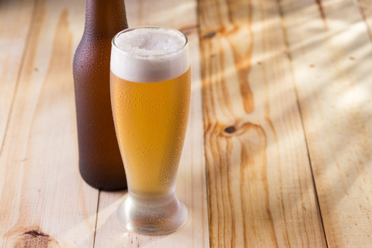 Tulipa de cerveja gelada e garrafa em mesa de madeira