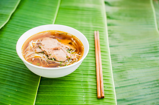 A bowl of Traditional Vietnamese beef soup Pho Bo on banana leaf background.