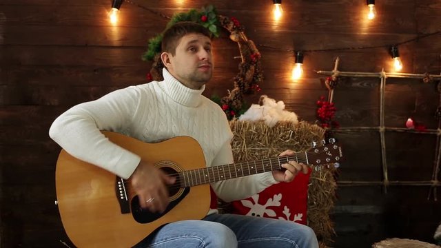 Man playing guitar on a Christmas background. Guy playing the guitar. A man plays the guitar and sings.