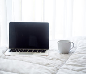 The laptop and coffee in the morning on a white bed, soft and select focus