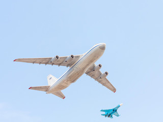 An-124 Ruslan cargo strategic airlift jet and Su-27 jet fighter fly against blue sky background
