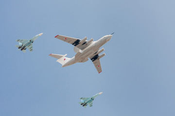 A-50 (AWACS) aircraft escorted by two Su-27 jet fighters flies against blue sky background

