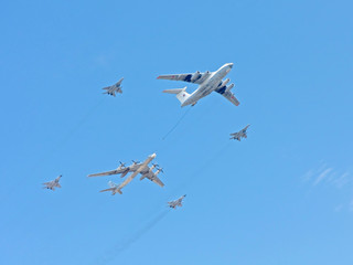 Il-78 aerial refueling tanker with Tu-95 strategic bomber and Mig-29 jet fighter fly against blue sky background
