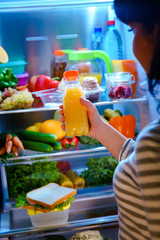 Woman takes the Orange juice from the open refrigerator