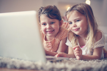 Two little sisters lying on the floor at living room and using l