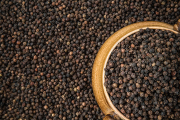 Black pepper grain in the bowl on the pepper background. Healthy eating and lifestyle.