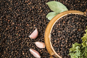Black pepper grain in the bowl on the pepper background with dried bay leaves, garlic and parsley. Healthy eating and lifestyle.