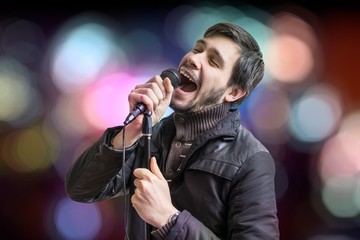 Karaoke concept. Young man holds microphone and singing a song on blurred background.