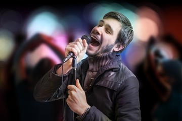 Young man is singing a song and people are dancing in club.
