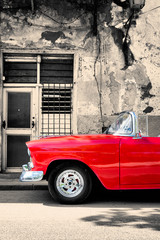Red vintage car next to a black and white building in Old Havana