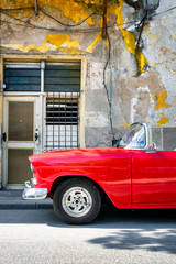 Classic red convertible car next to a shabby building in Old Havana