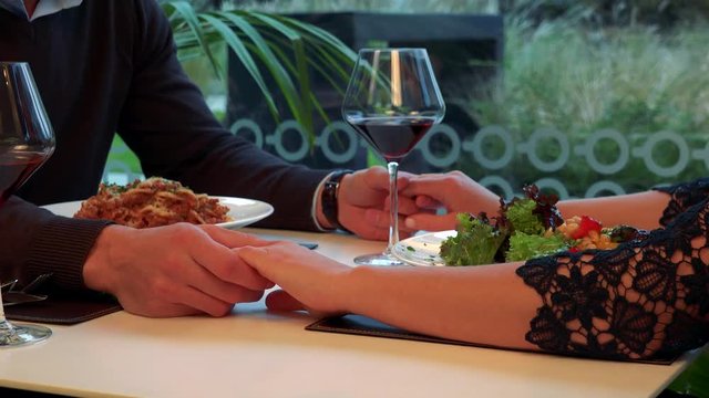 Male and female hands connected across a table with meal and wine