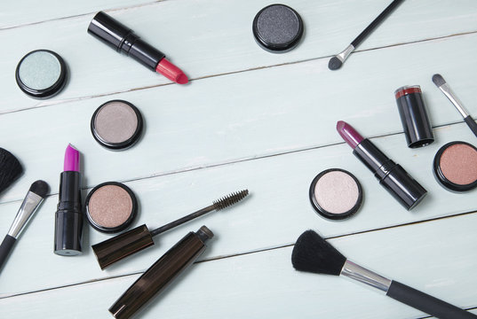 Make up and cosmetic beauty products strewn across a wooden dressing table background, with blank space in the middle