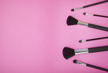 A selection of cosmetic make up brushes on a bright pink background with empty space at side