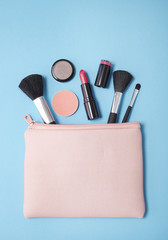 Aerial view of make up products spilling out of a pink cosmetics bag on to a blue background