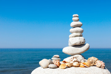 Fototapeta na wymiar pyramid of white stones and shells on a background of blue sky and sea