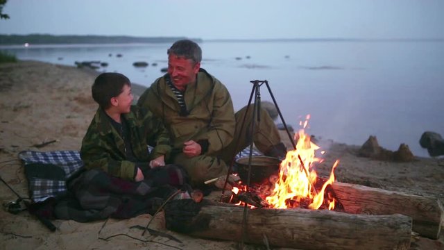 Father and son sitting around the campfire at the lake.