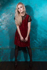 Naklejka premium Beautiful blonde girl in a red dress posing against a wall green