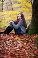 Pretty young girl sitting on dried leaves in a forrest