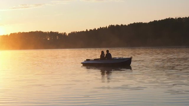 A loving couple riding on a rowing boat on the river in time of golden sunset. The golden light of the sun on the water surface of the lake. Golden sunset sunrise on the lake.
