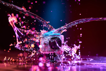 Concept: gear, gadget, action lifestyle, millennial. Vivid colorful shot of action camera in waterproof case splashed with water. Time freeze.