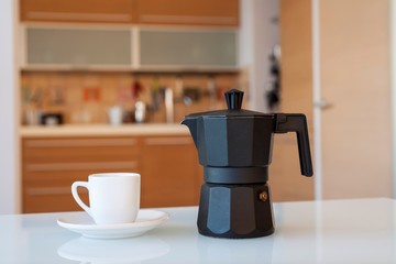 чашка и кофейник на столе на фоне кухни