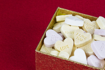Group of sweet candies with heart shape in a golden box in red background.