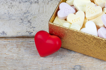 Group of sweet candies with heart shape in a golden box with red heart figure on a wooden table.