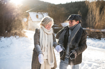 Beautiful senior couple blowing snow in sunny winter nature