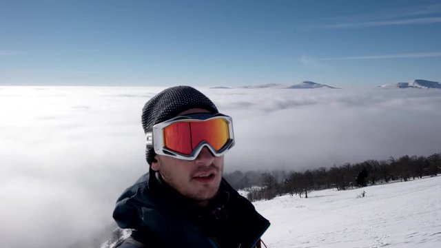 Man in Snow Mask is Making Selfie While Winter Hike Above the Clouds With a View of the Distant Peaks by a Coast of the Cloud Sea